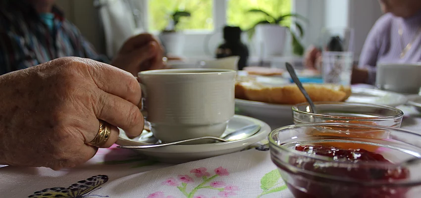 Die Hand einer alten Person greift nach einer Kaffeetasse an einem deckten Frühstückstisch