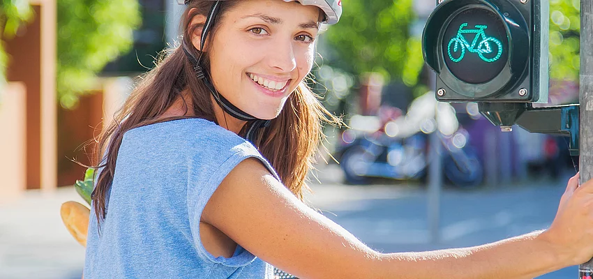 Eine Fahrradfahrerin macht auf die Aktion STADTRADELN aufmerksam. Eine Fahrradfahrerin mit Helm hält sich an einer Ampel fest.