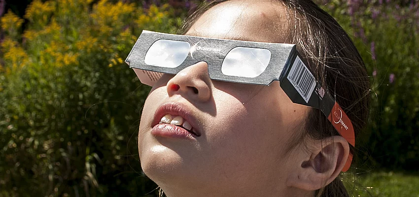 Mädchen schaut mit Schutzbrille zur Sonne Ein Mädchen mit einer Schutzbrille schaut zur Sonne.