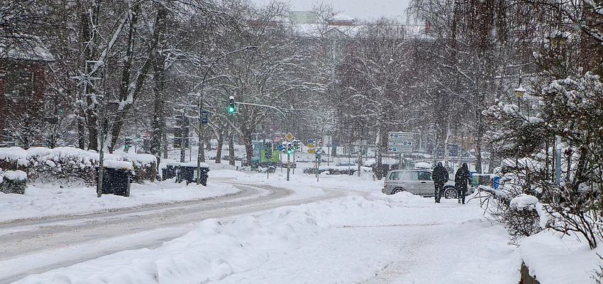 Es schneit, Menschen gehen den Oher Weg entlang und ein Auto biegt in eine Auffahrt ab.