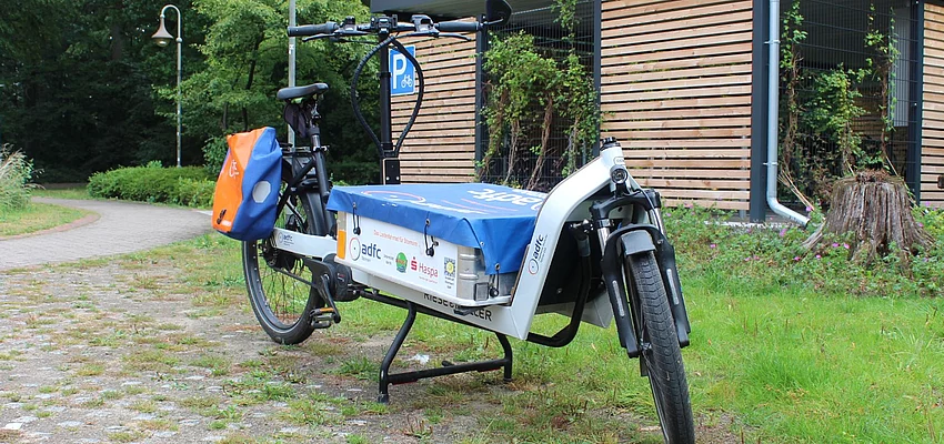 E-Lastenrad der Stadt Glinde Ein Fahrrad mit einem großen flachen Behälter hinter dem Vorderrad für Lasten.