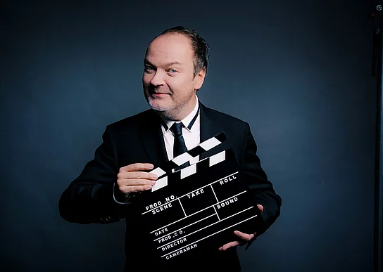 Jens Wawrczeck liest Hitchcock Ein Mann mit Halbglatze hat eine Filmklappe vor sich.