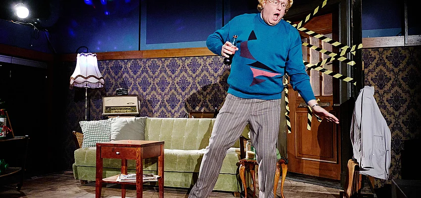 Ein Mann mit blauem Pullover tanzt in einem Wohnzimmer.